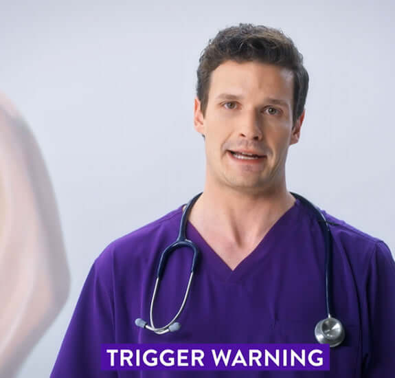Male healthcare professional in purple scrubs giving a trigger warning, with a stethoscope around his neck.
