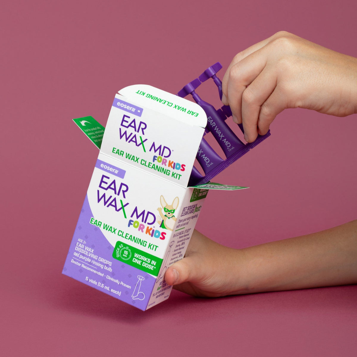 Child hand holding an 'EAR WAX MD for Kids' ear wax cleaning kit and pulling Ear Wax Vials out of the box. 