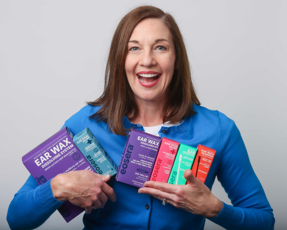 eosera founder Elyse Dickerson smiles, wearing a blue sweater, holding several eosera ear care products