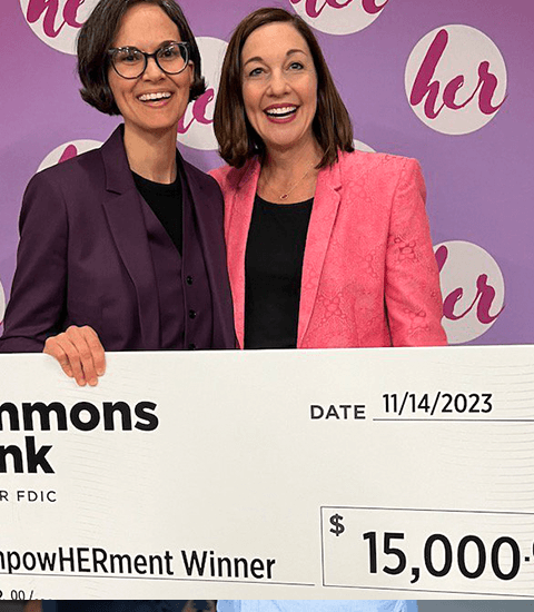 Two women smiling, holding a giant check from Simmons Bank for the EmpowerHERment Program, dated 11/14/2023.